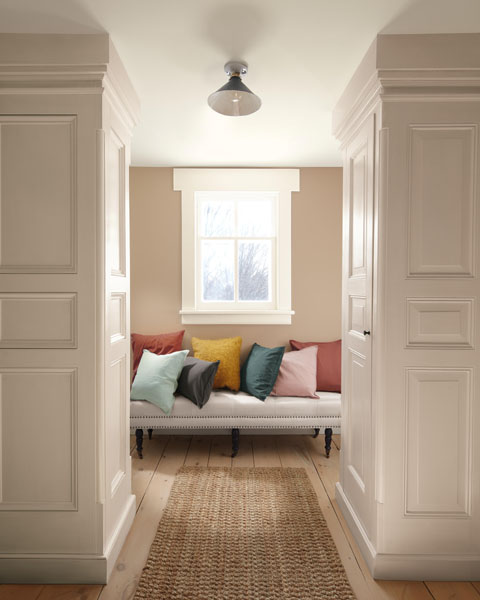 A vignette featuring a contemporary bench with colourful cushions. The walls are painted in Sherwood Tan 1054 and the panelling is painted in First Crush CSP-310.
